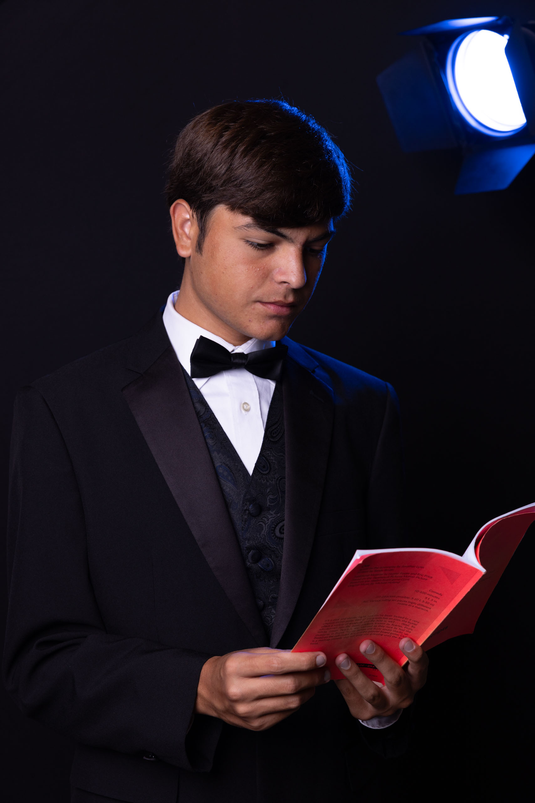 Teenage boy in tuxedo with script and theater lighting
